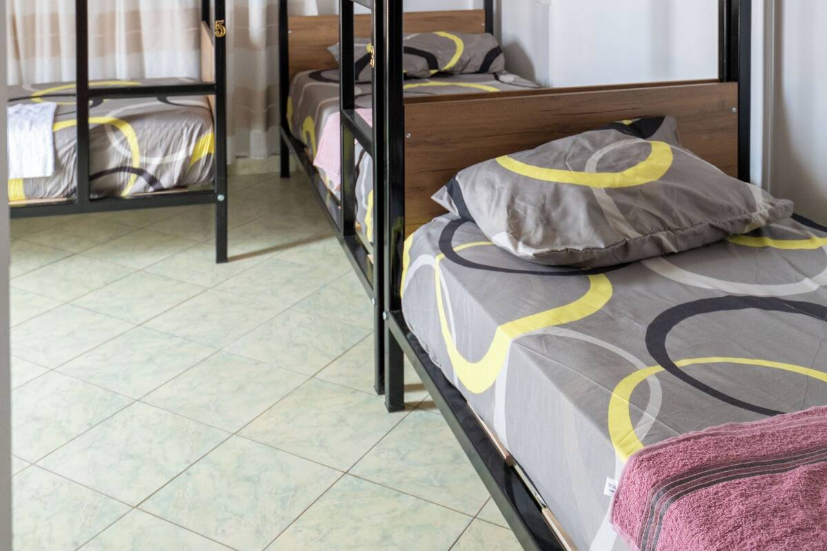A dormitory room with bunk beds, a curtain, and a tiled floor.