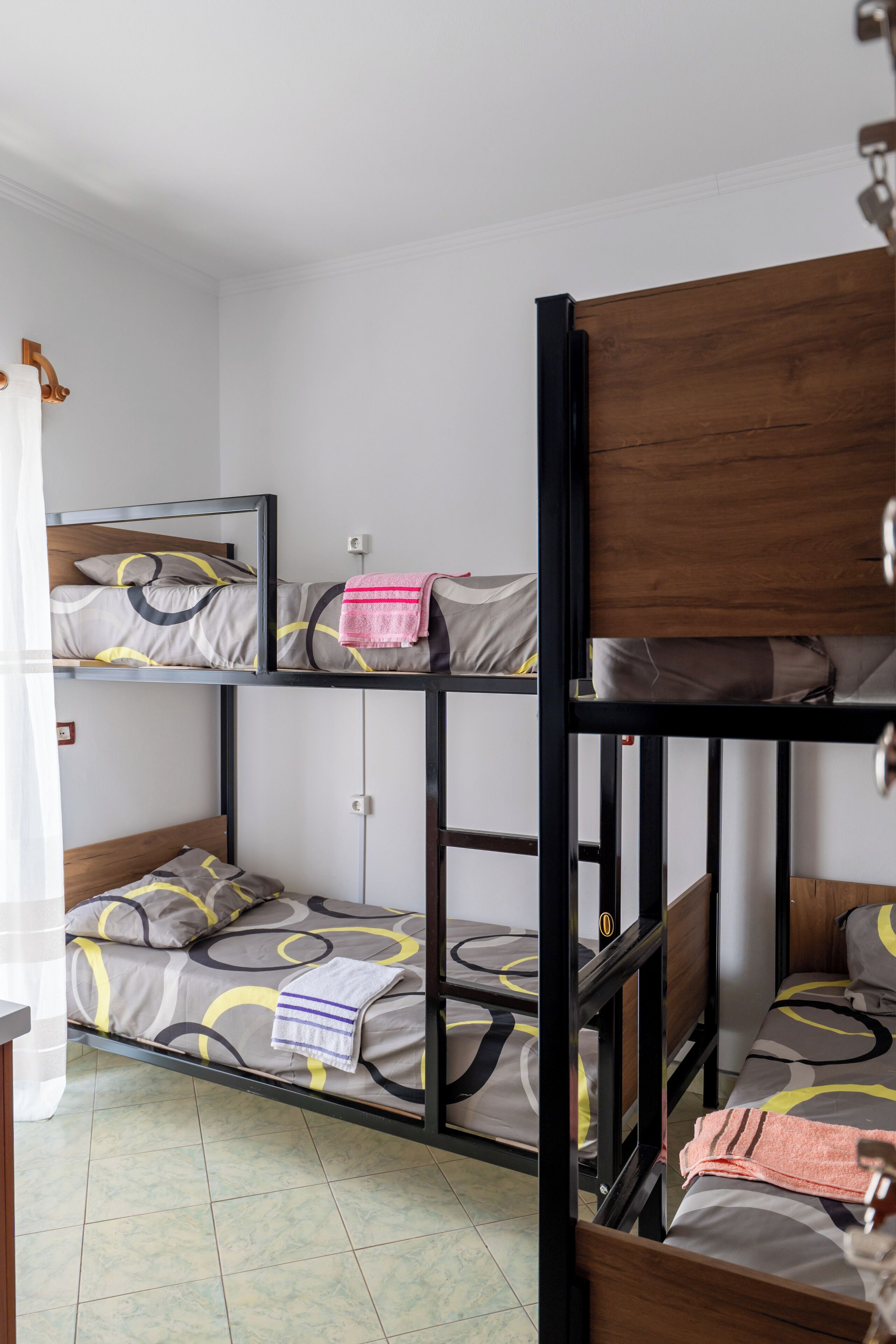 A bunk bed room with a wooden frame, two beds with patterned bedding, and a curtain on the left.