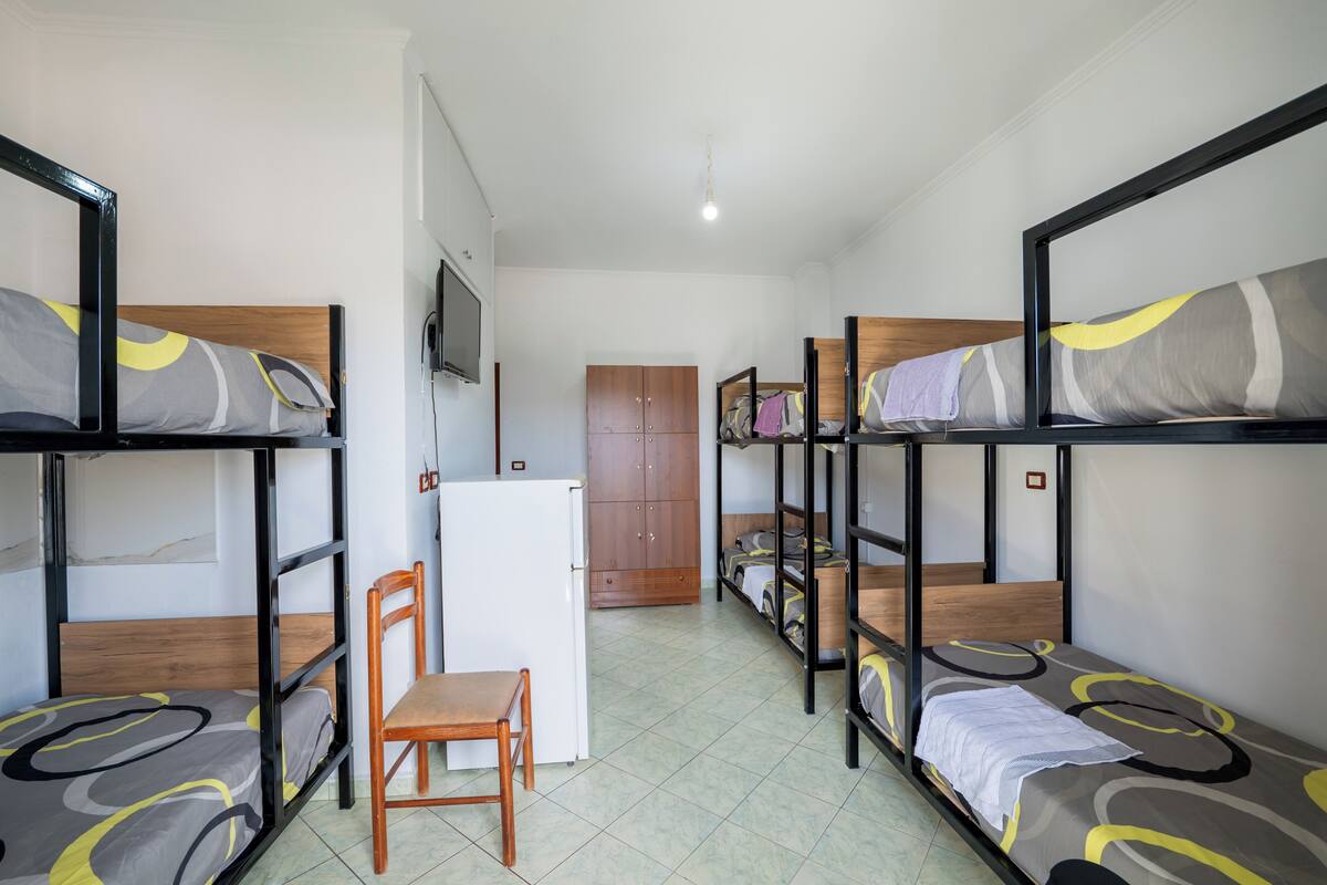 A dormitory room with bunk beds, a small desk, and a chair.