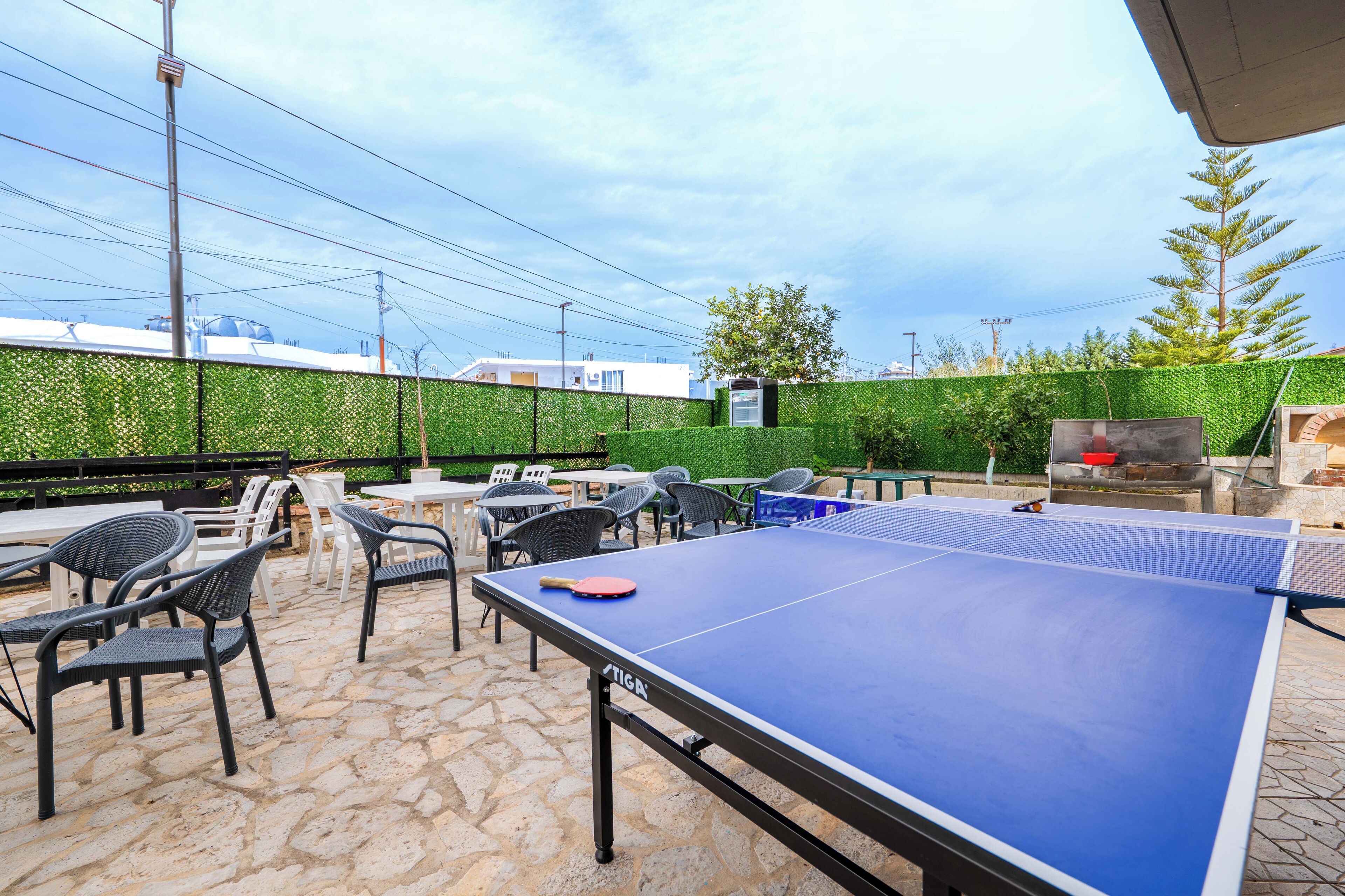 An outdoor ping pong table with chairs and a barbecue area.