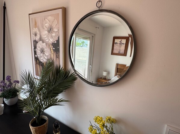 A mirror reflecting a room with a bed, a nightstand, and a framed picture on the wall.