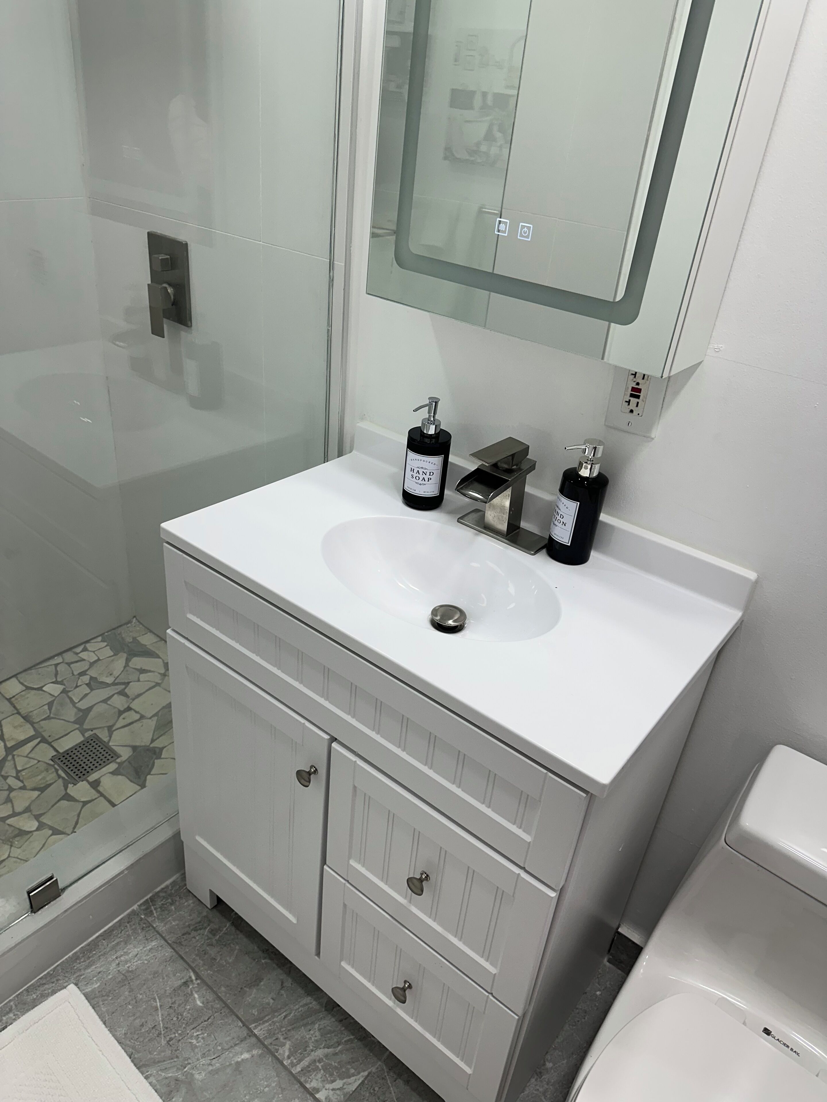 Un bagno moderno con un lavandino bianco, due erogatori di sapone neri, uno specchio sopra il lavandino e un water bianco.