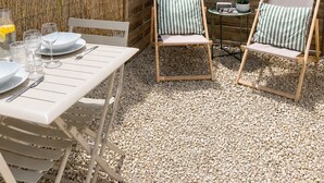 A patio with a table set for dining, two striped lounge chairs, and a wooden fence with hanging planters. - La Vie Douce - Between Ocean & Marshes (Saint-Michel-en-l'Herm)