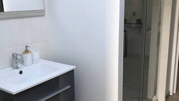 Un baño moderno con un lavabo blanco, un mueble oscuro y un box de ducha de vidrio.