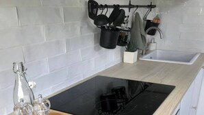 A modern kitchen with a black induction cooktop, a wooden tray with salt and pepper shakers, and a hanging pot rack above the sink. - La Vie Douce - Between Ocean & Marshes (Saint-Michel-en-l'Herm)