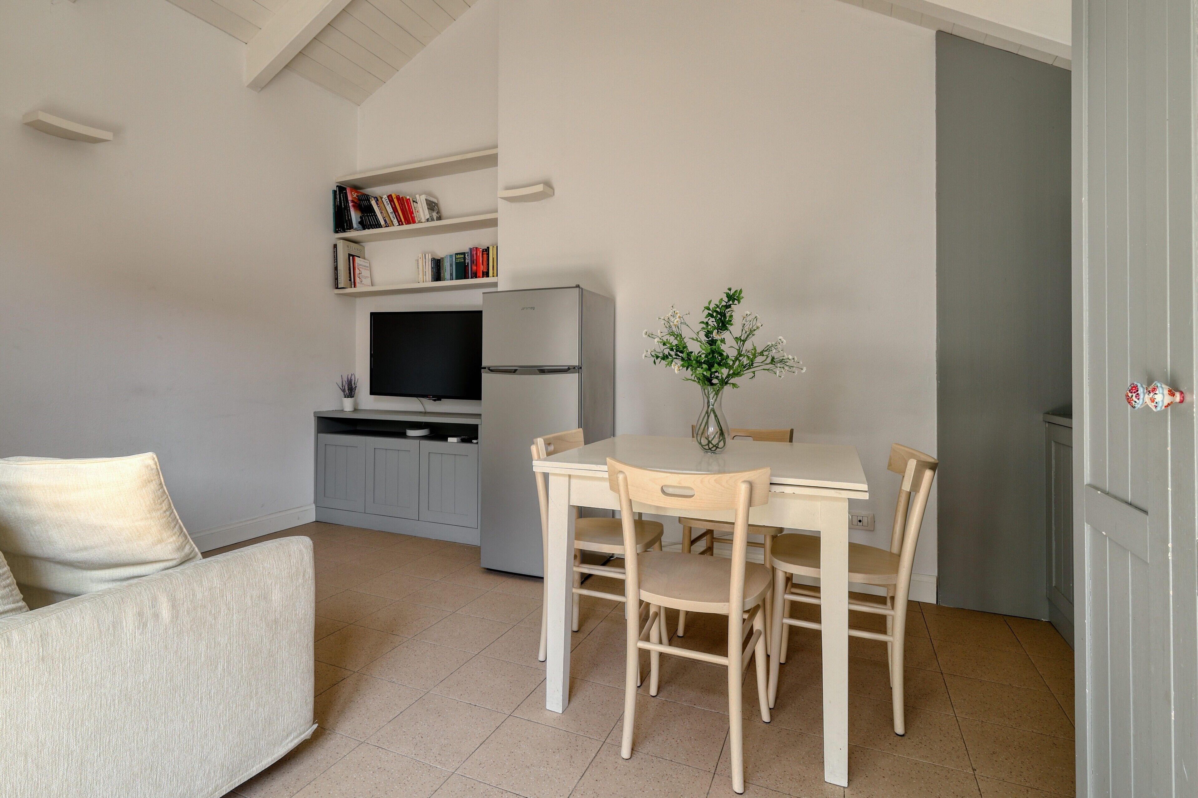 A compact living space with a dining table, chairs, a sofa, a television, a refrigerator, and a bookshelf.