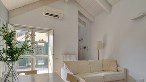 A room with a white sofa, a wooden chair, a table, a vase with greenery, and a window with blinds.