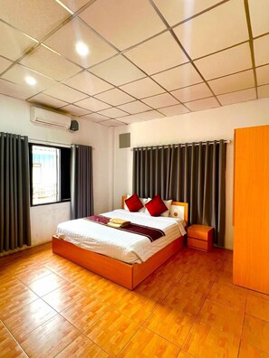 A hotel room with a wooden bed, a nightstand, a wardrobe, and a window with curtains.