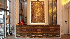 A reception desk with a large, striped marble top, flanked by tall, white columns and a large, ornate wall panel. - Elite World Nest Sivas (Sivas)