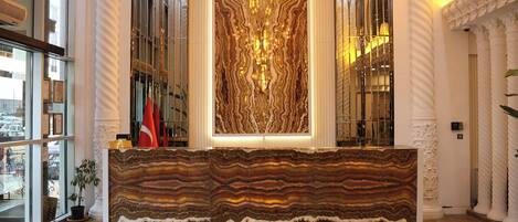 Un mostrador de recepción con una gran superficie de mármol a rayas, flanqueado por altas columnas blancas y un panel de pared grande y ornamentado.