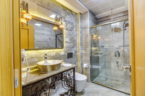 Un baño moderno con un lavabo de mármol, cabina de ducha con paredes de vidrio y apliques de pared decorativos.