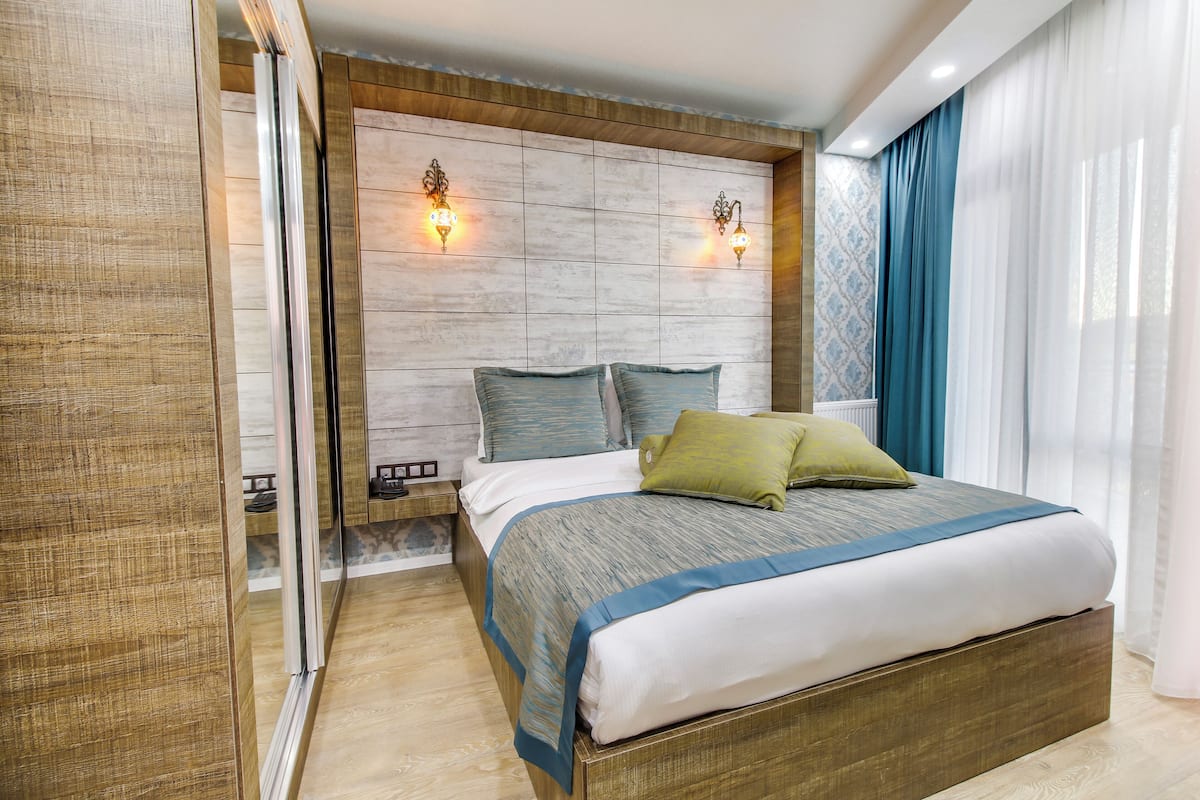 Un dormitorio moderno con una cama grande, cabecera de madera y dos luces fijadas a la pared.