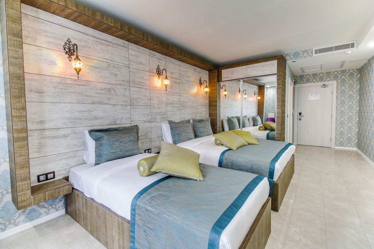 Habitación de hotel con dos camas, cabecero de madera, apliques de pared y un espejo grande.