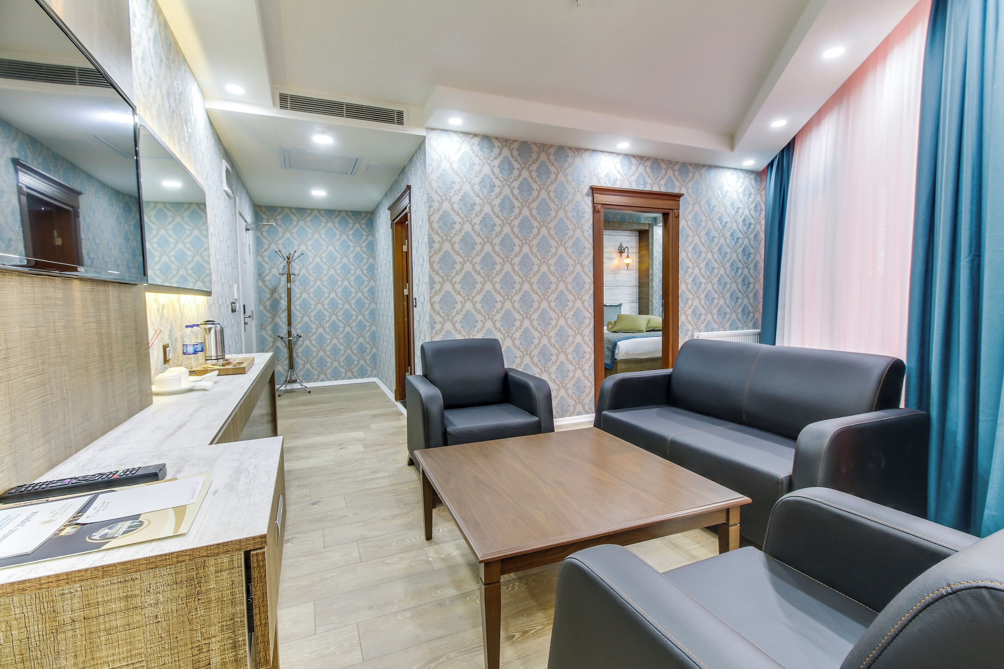 A hotel room with a wooden reception desk, a sofa, a table, and a mirror.