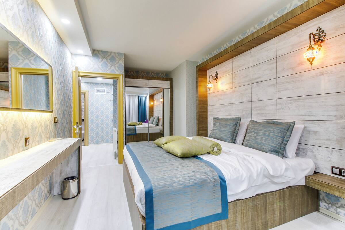 Una habitación de hotel moderna con una cama grande, un tocador con espejo y un cabecero de madera.