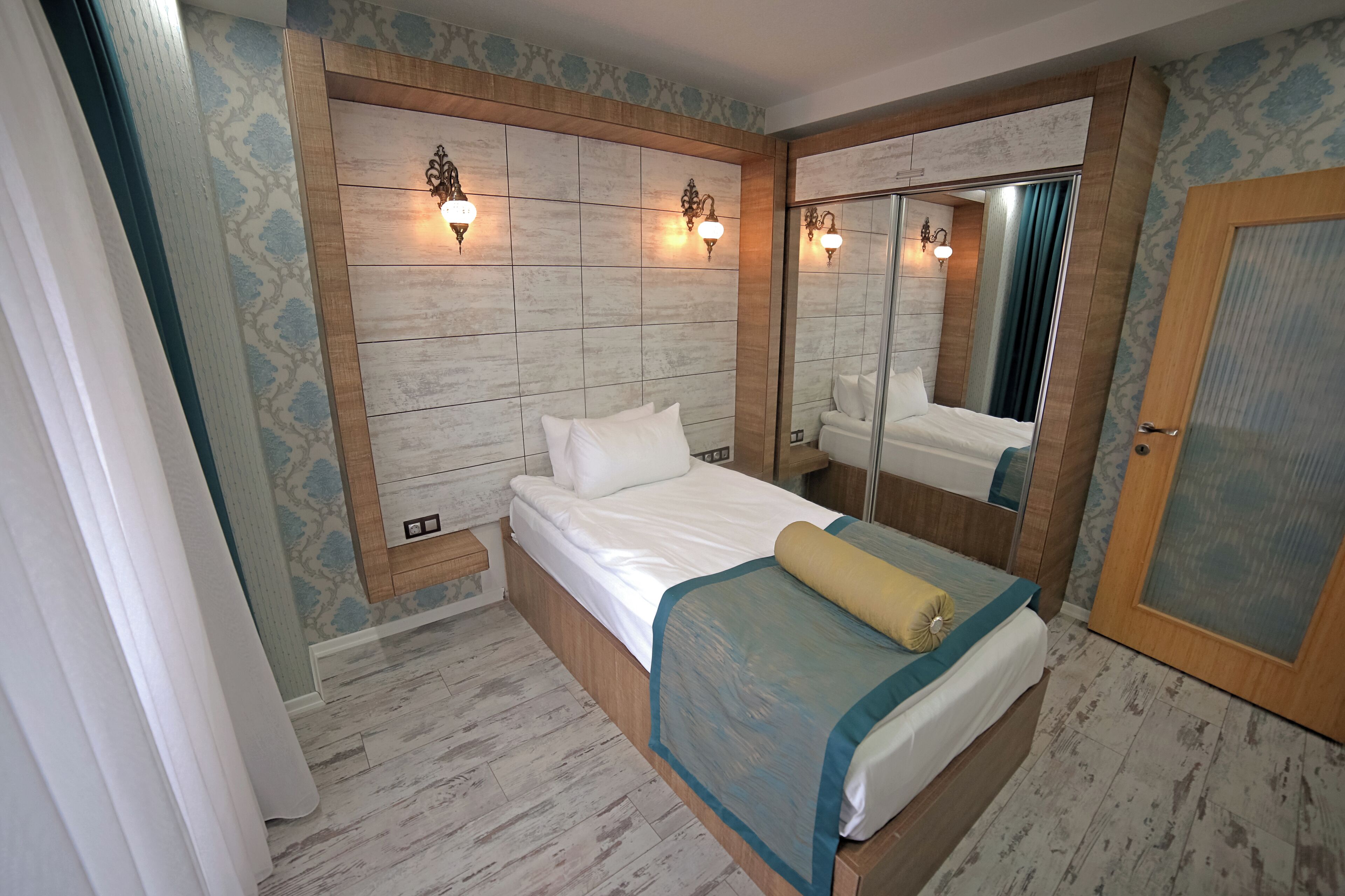 Un dormitorio con cabecera de madera, cama con ropa de cama blanca, mesita de noche y un espejo.