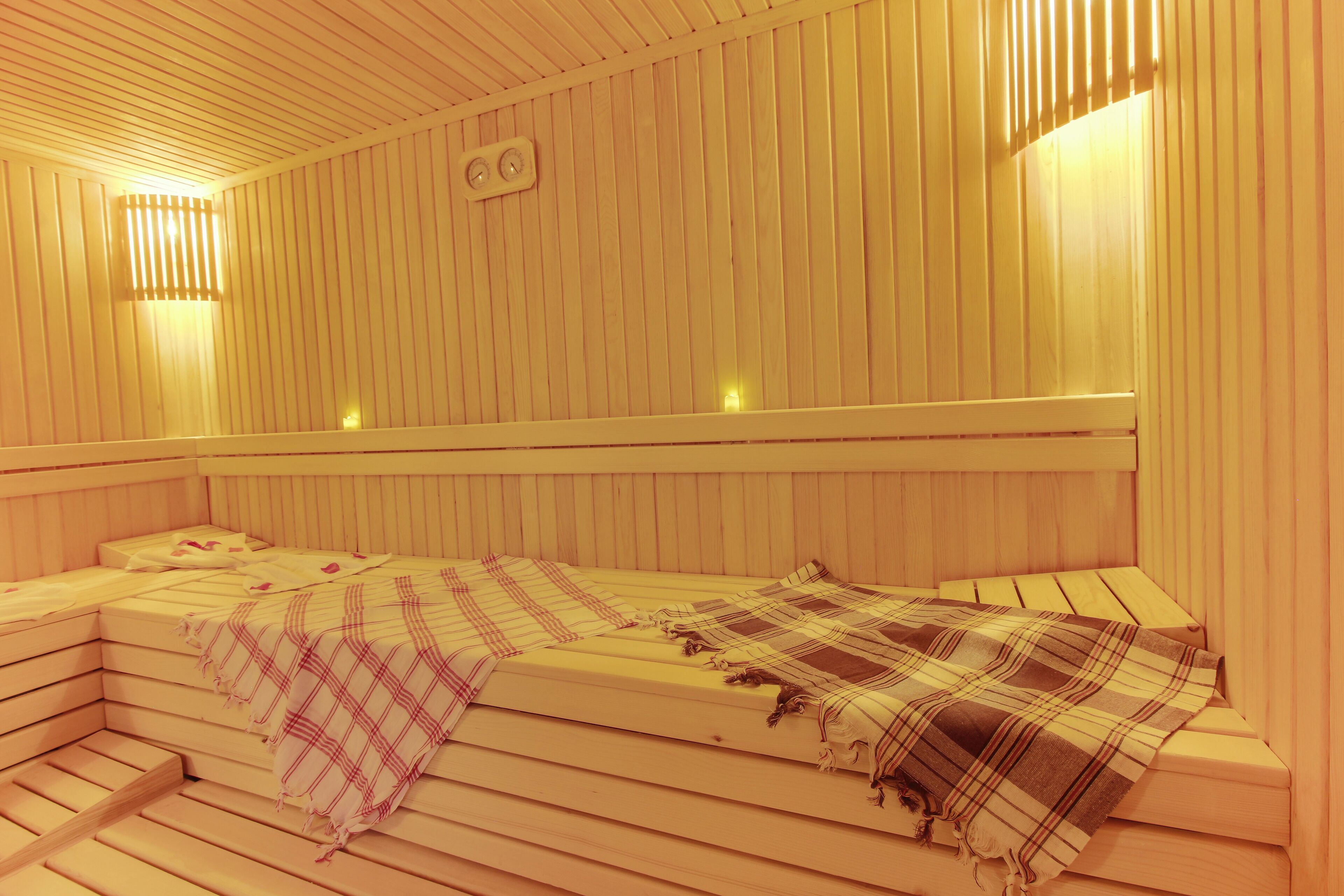 A sauna with two benches, wooden walls, and wall-mounted lights.