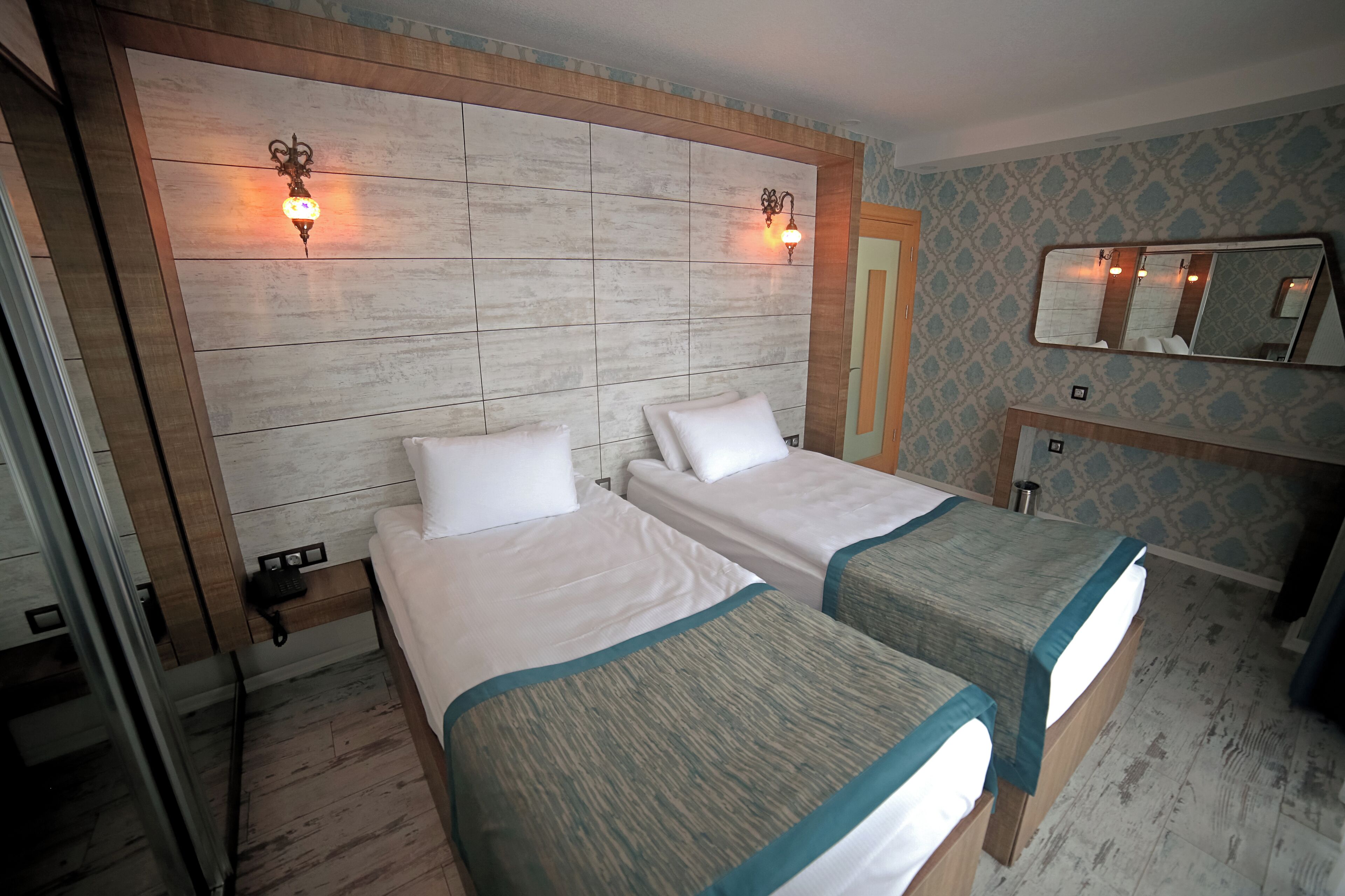 Une chambre d’hôtel avec deux lits, une tête de lit en bois, des lampes fixées au mur, un miroir et une petite table de chevet.