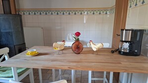 Una cucina con un tavolo di legno, sedie bianche, una macchina da caffè e figurine decorative a forma di gallina.