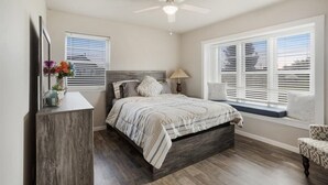 A bedroom with a bed, a bedside table, a lamp, and a window with blinds.
