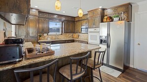 A kitchen with wooden cabinets, a central island with bar stools, a refrigerator, and pendant lighting.