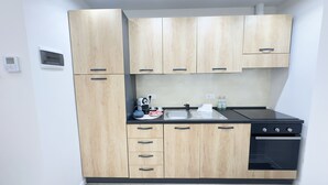 Een kleine keuken met houten kastjes, een zwart aanrechtblad, een waterkoker, een koffiezetapparaat en een spoelbak.