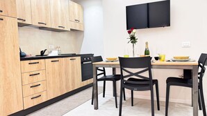 Een moderne keuken met houten kastjes, een zwarte kookplaat en een eethoek met tafel en stoelen.