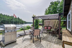 Enjoy al fresco dining with a grill and comfortable outdoor seating under a shaded pergola overlooking the serene lake.