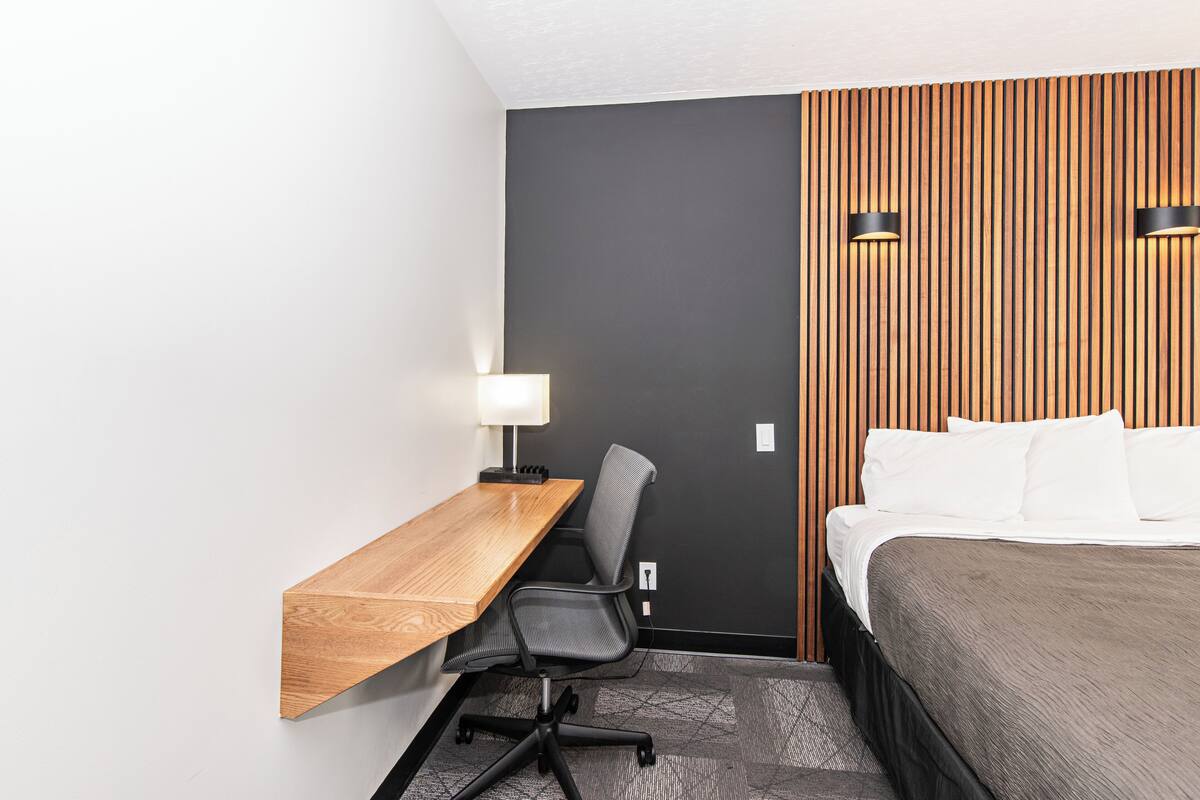 Une chambre d’hôtel avec un bureau en bois, une chaise, un lit et un mur recouvert de lattes de bois verticales.