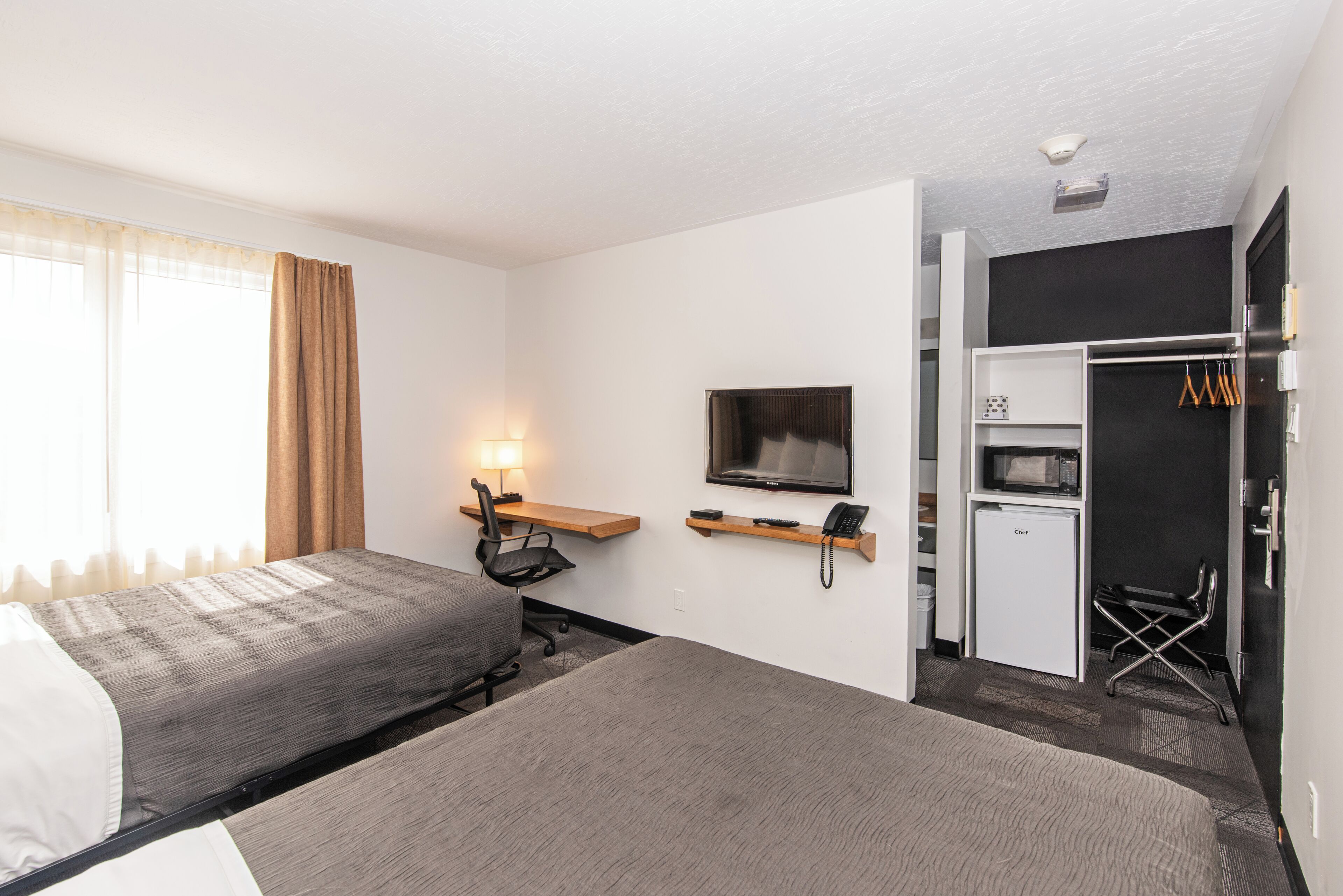 A hotel room with a bed, desk, chair, TV, and a mini-fridge.