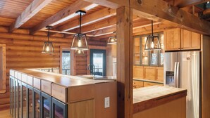 Een houten chalet van binnen met een ruime keuken, houten balken in het plafond en hanglampen.