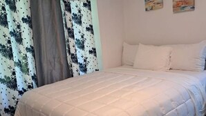 A bedroom with a bed, white bedding, and a window with patterned curtains. - 4-bedroom house (118, Trois-Rivières,)