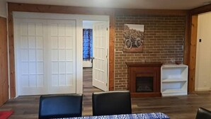 A room with a fireplace, a door, and a table with chairs. - 4-bedroom house (118, Trois-Rivières,)