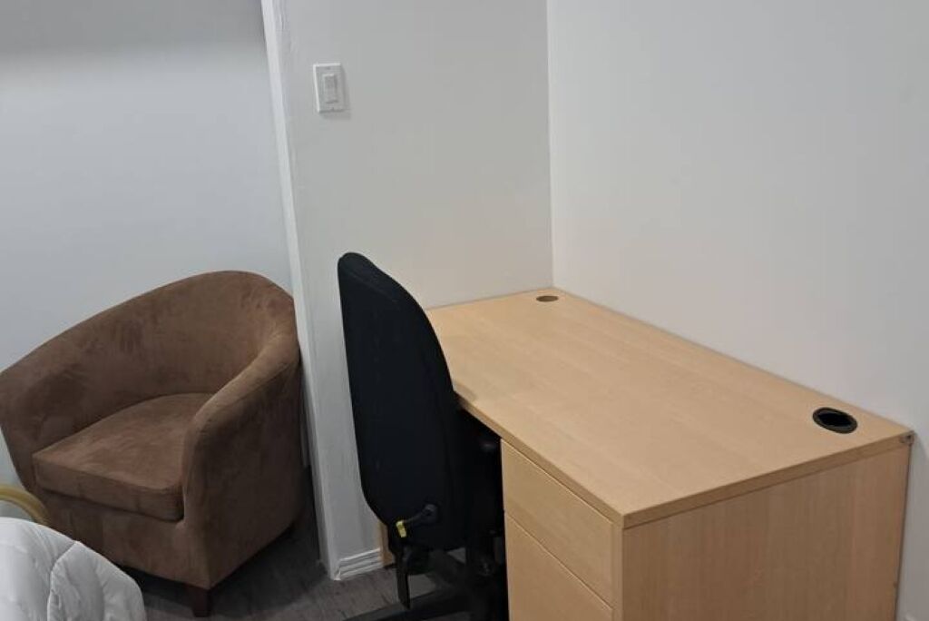 A small room with a brown chair, a black office chair, and a wooden desk.
