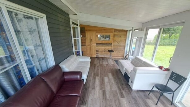 A modern interior with a wooden wall, a white sofa, a brown leather sofa, and a chair. - 4-bedroom house (118, Trois-Rivières,)