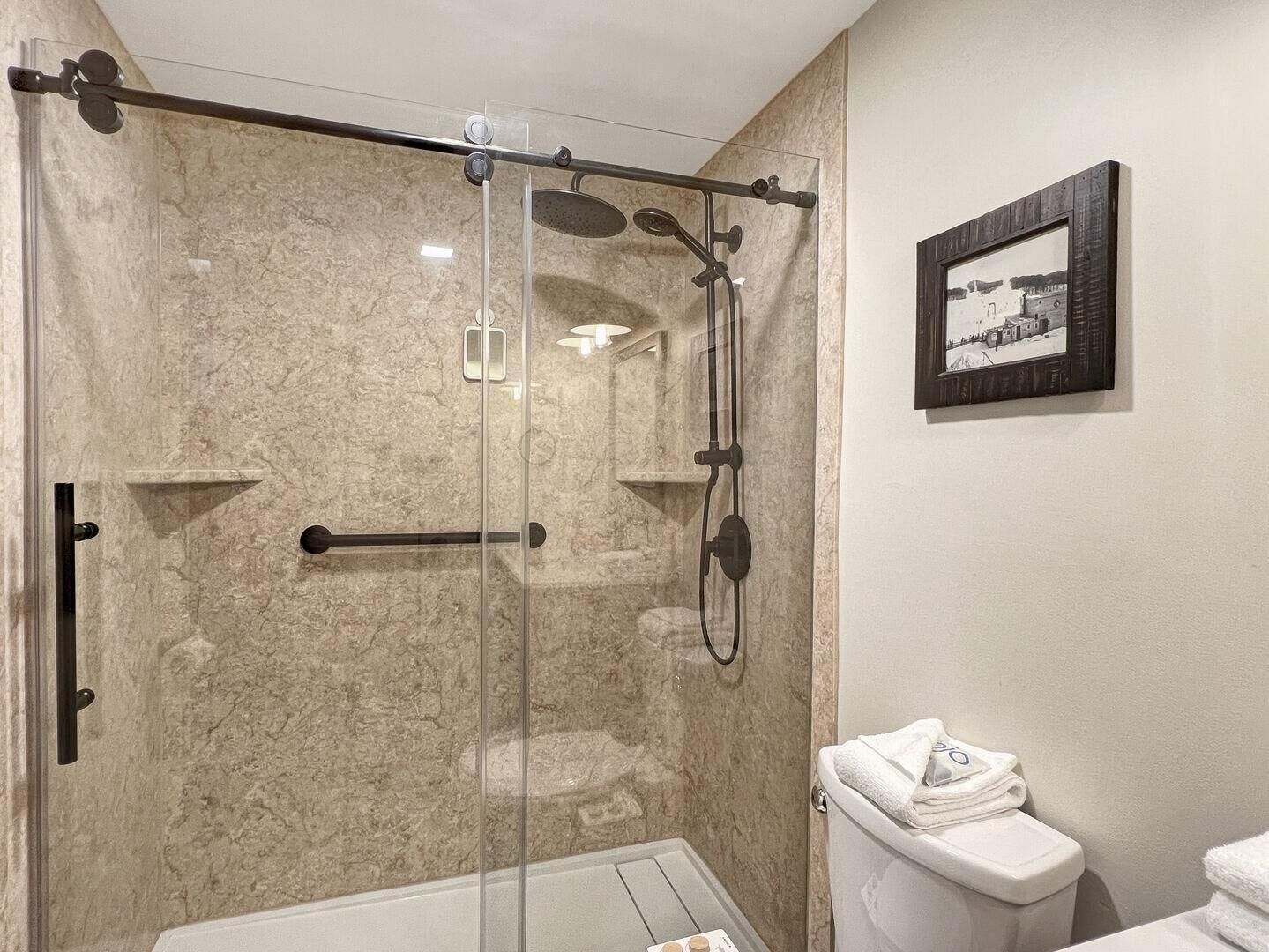 A modern bathroom with a glass-enclosed shower, a toilet, and a framed picture on the wall.