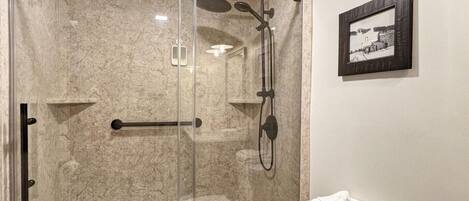 A modern bathroom with a glass-enclosed shower, a toilet, and a framed picture on the wall.