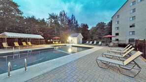 A swimming pool with lounge chairs and umbrellas, surrounded by a building and trees. - Mt Green 3-d10 (Killington)