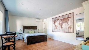 A bedroom with a wooden floor, a bed with a headboard, a desk with a chair, a large world map artwork, and a window. - Beautiful 1 Bedroom, 1 Bathroom in Medford with WiFi and AC (Medford)
