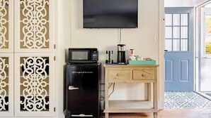 A room with a flat-screen TV mounted on the wall, a black refrigerator with a microwave on top, a coffee maker, and a small wooden desk with drawers. - Beautiful 1 Bedroom, 1 Bathroom in Medford with WiFi and AC (Medford)