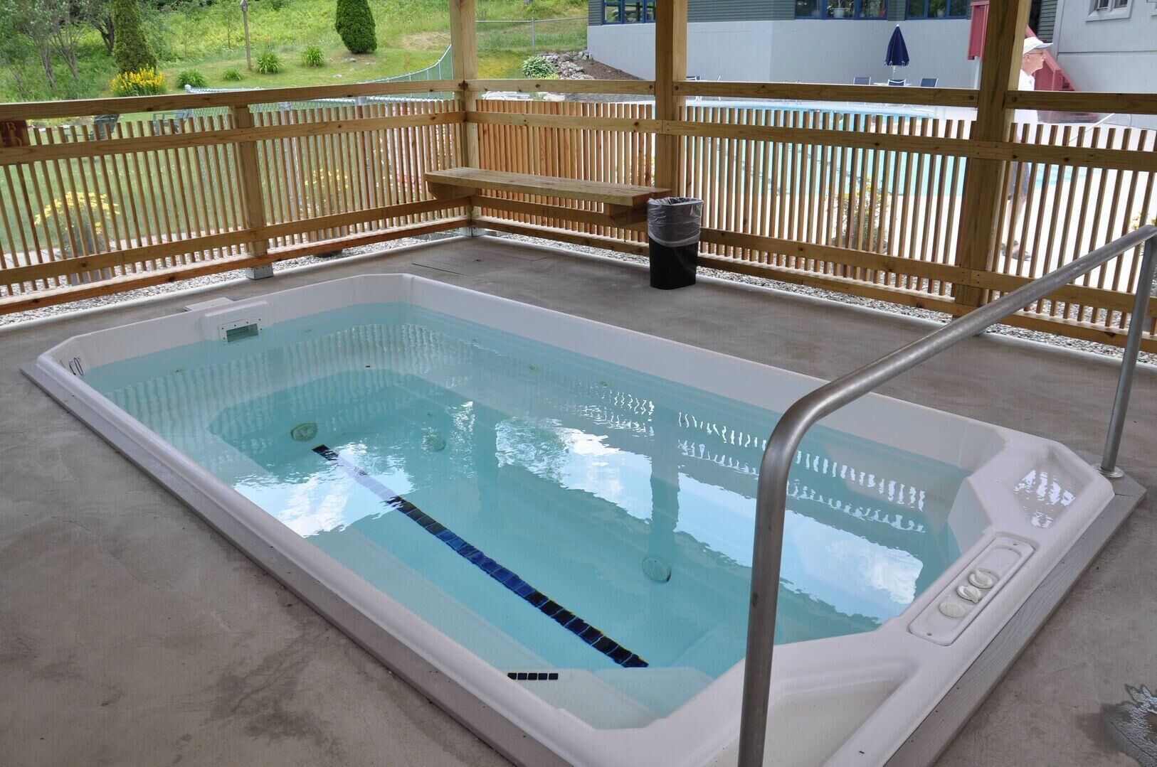 Une piscine extérieure rectangulaire, dotée d’une terrasse en bois et d’une échelle en métal.