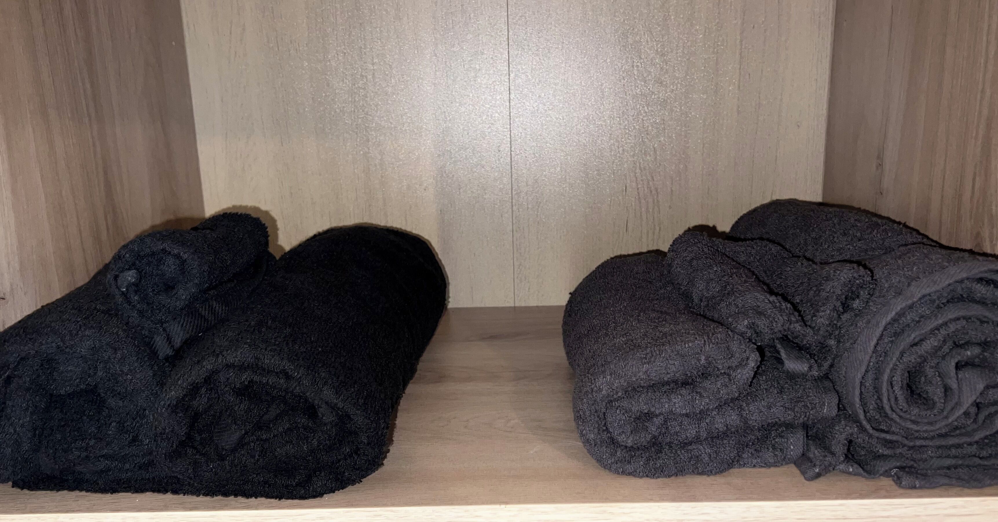 A wooden shelf with two rolled-up black towels.