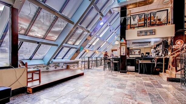 Un restaurante con techo alto y tragaluces, una zona de bar y un área de comedor con mesas y sillas.