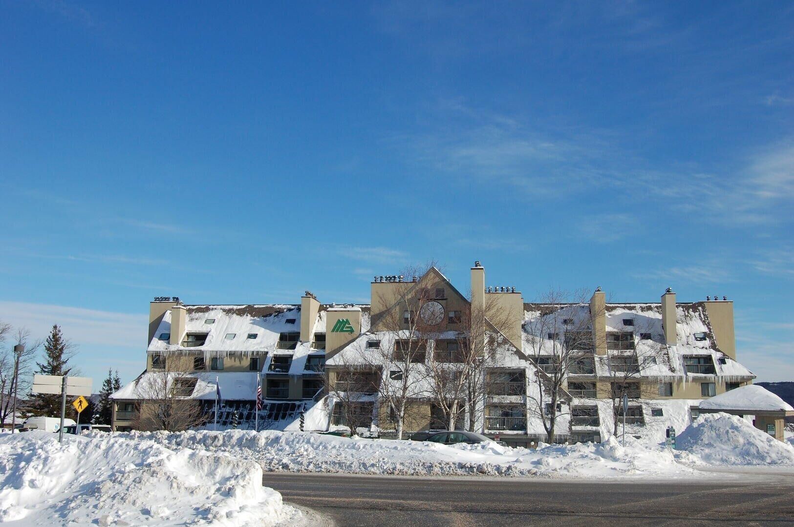 Un hotel de varios pisos con una torre central de reloj, rodeado de edificios cubiertos de nieve.