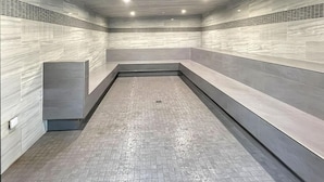 Un baño moderno con azulejos, zona de ducha rectangular y bancos a lo largo de las paredes.