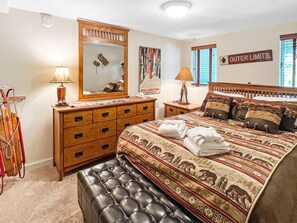 A bedroom with a large bed, a wooden dresser, a mirror, and a sign indicating 'Outer Limits'. - Sunrise Northstar B1 - Bear View (Killington)