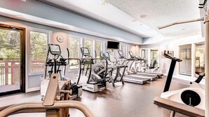 Un gimnasio con diferentes máquinas de cardio, ventanas amplias y vistas al exterior.