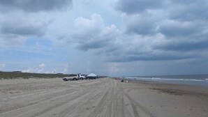 Una playa con vehículos y tiendas de campaña, terreno arenoso y cielo nublado.