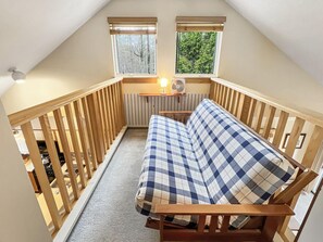 A loft bedroom with a checkered mattress, wooden railing, and two windows with blinds.