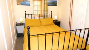 A bed with a metal frame and yellow bedding, two bedside lamps, and two landscape paintings on the wall. - Tryfan Cottage  -  2.8 miles from Summit of Mt Snowdon (Beddgelert)